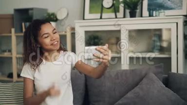 微笑着年轻的非洲裔美国妇女正在做在线视频电话，看着智能手机屏幕谈笑风生
